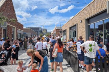 Crowds enjoying a summer community event at Waverley, with outdoor seating, shops and The Canary bar visible along the pedestrian street.